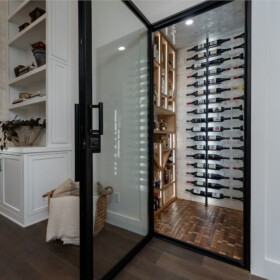 A metal pull handle allows users to open this modern wine cellar's glass door.